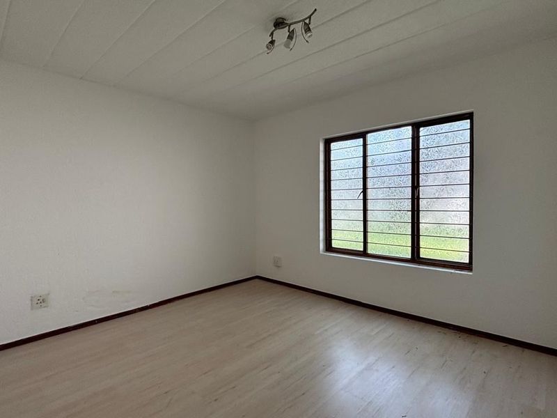 An empty bedroom featuring laminate flooring, a window with security bars, and a built-in cupboard, ready for personalization.