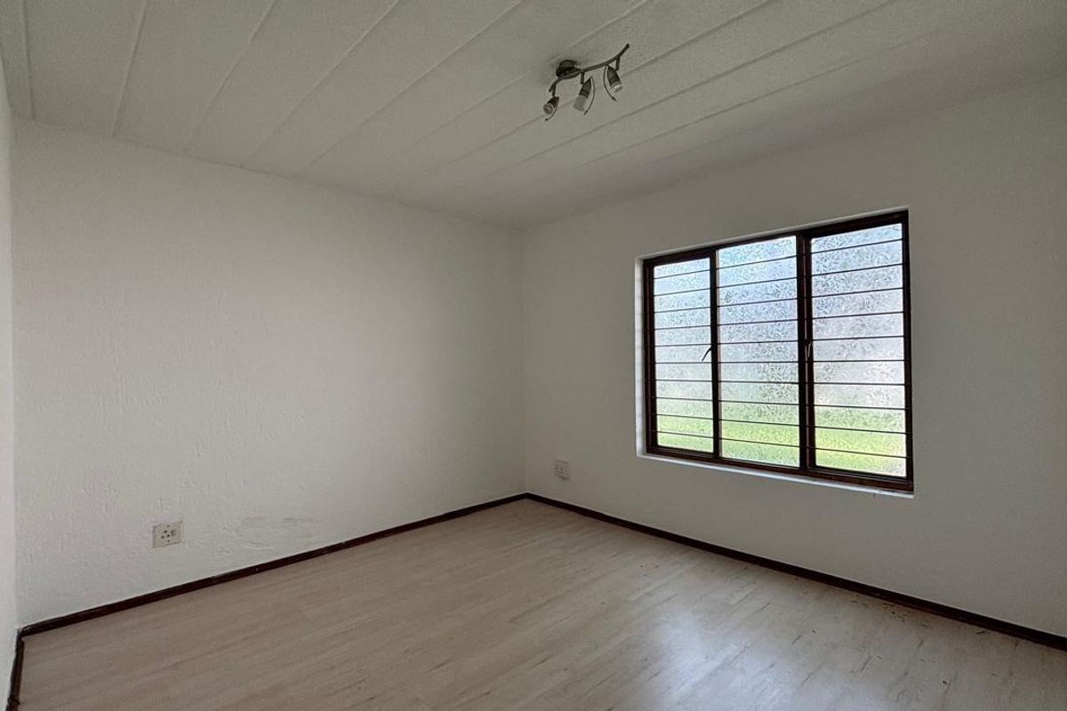 A vacant bedroom featuring laminate flooring, a window with security bars, and a simple ceiling light fixture, offering a clean canvas for personalization.