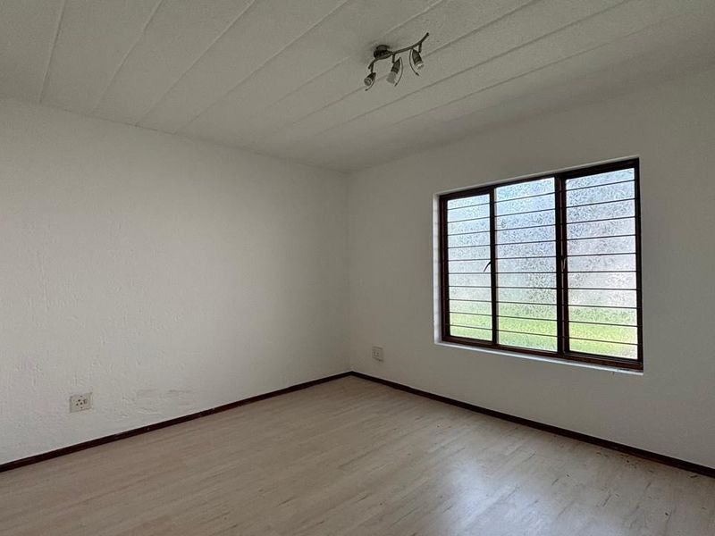 A vacant bedroom featuring laminate flooring, a window with security bars, and a simple ceiling light fixture, offering a clean canvas for personalization.