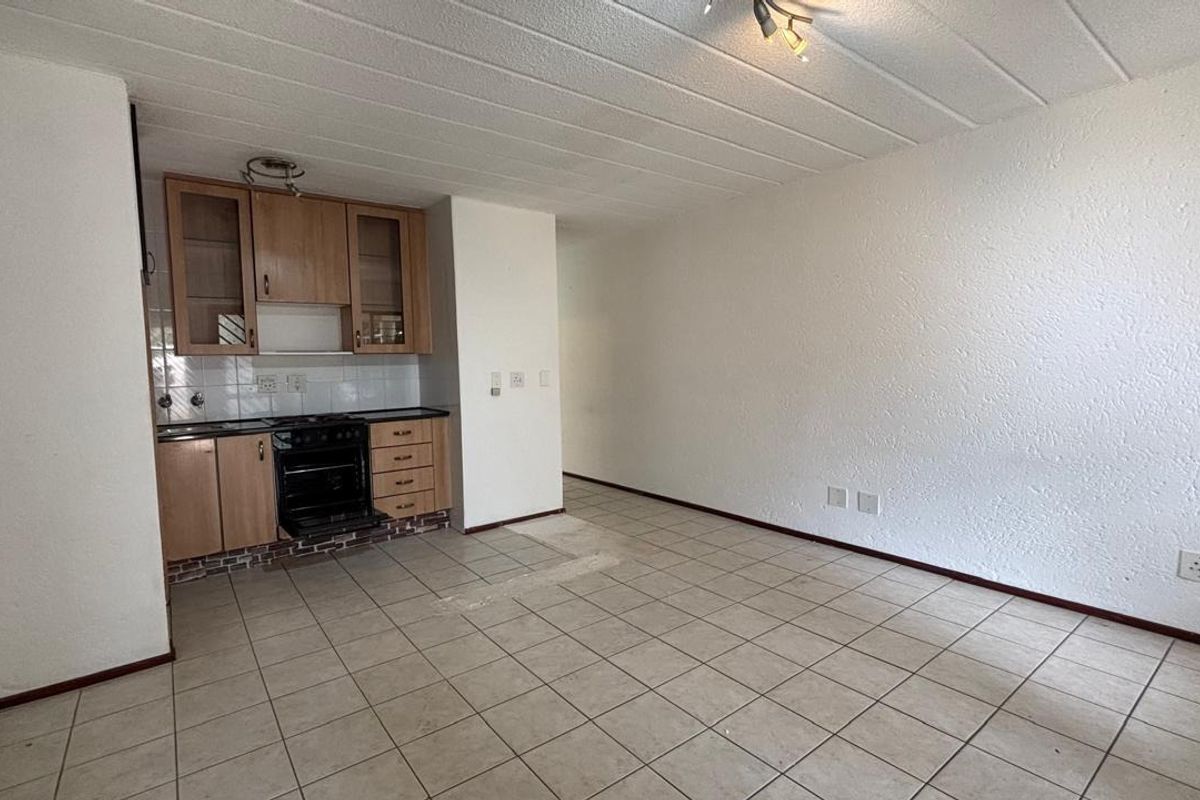 An open-plan living and kitchen area featuring tiled flooring, textured ceilings, and dated built-in cabinetry with an integrated oven.
