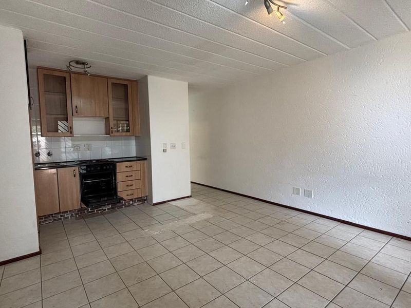 An open-plan living and kitchen area featuring tiled flooring, textured ceilings, and dated built-in cabinetry with an integrated oven.