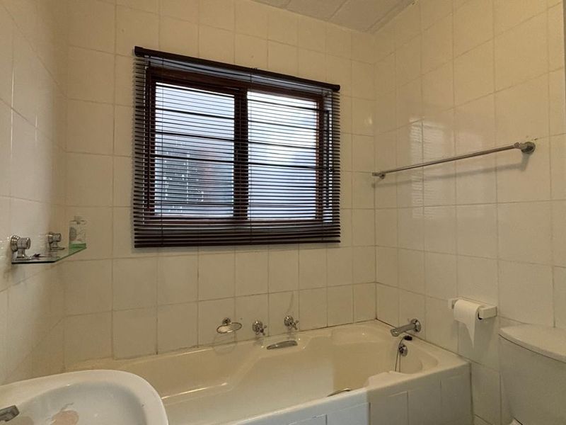 A dated bathroom featuring a built-in bathtub, pedestal basin, and full-height ceramic wall tiling, offering a blank canvas for modern renovation.