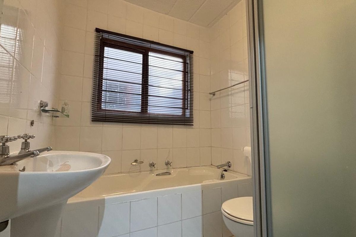 A functional bathroom featuring a pedestal basin, built-in bathtub, toilet, and a separate shower enclosure with white wall tiling.