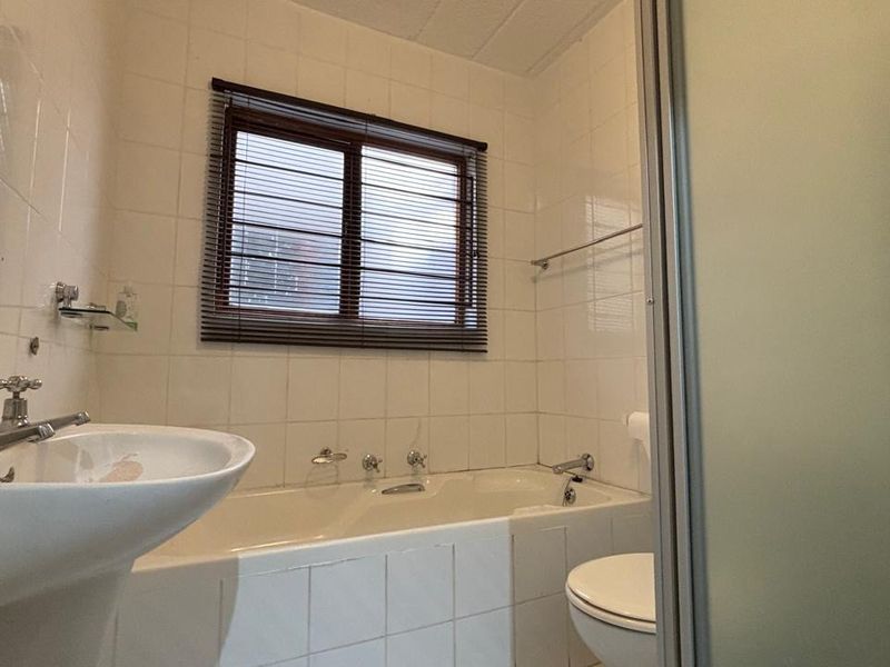 A functional bathroom featuring a pedestal basin, built-in bathtub, toilet, and a separate shower enclosure with white wall tiling.