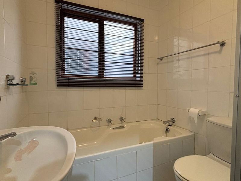 A functional bathroom featuring a bathtub, pedestal basin, and toilet with white wall tiling and a window for natural light.