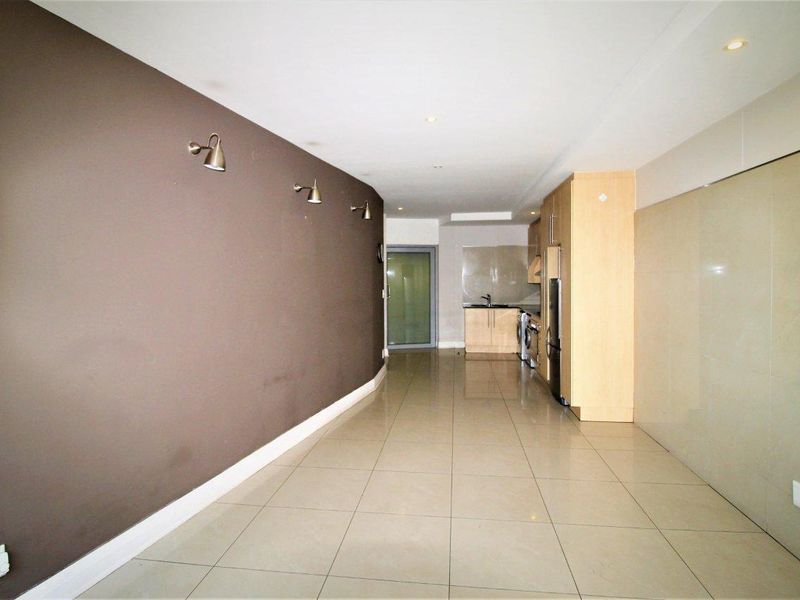 An open-plan living and kitchen area featuring tiled flooring, recessed lighting, and modern built-in cabinetry in a clean, vacant space.