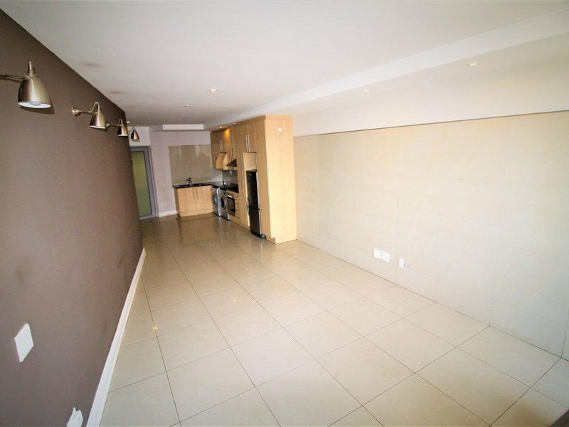 Spacious open-plan living area featuring tiled flooring, recessed lighting, and a compact built-in kitchen with integrated appliances.