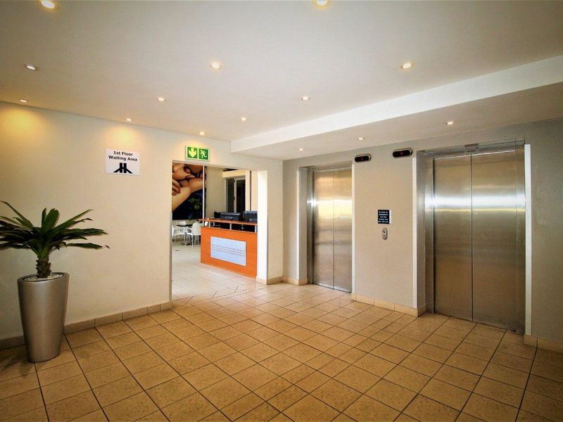 A clean and professional apartment building lobby featuring stainless steel elevators, tiled flooring, and recessed lighting.