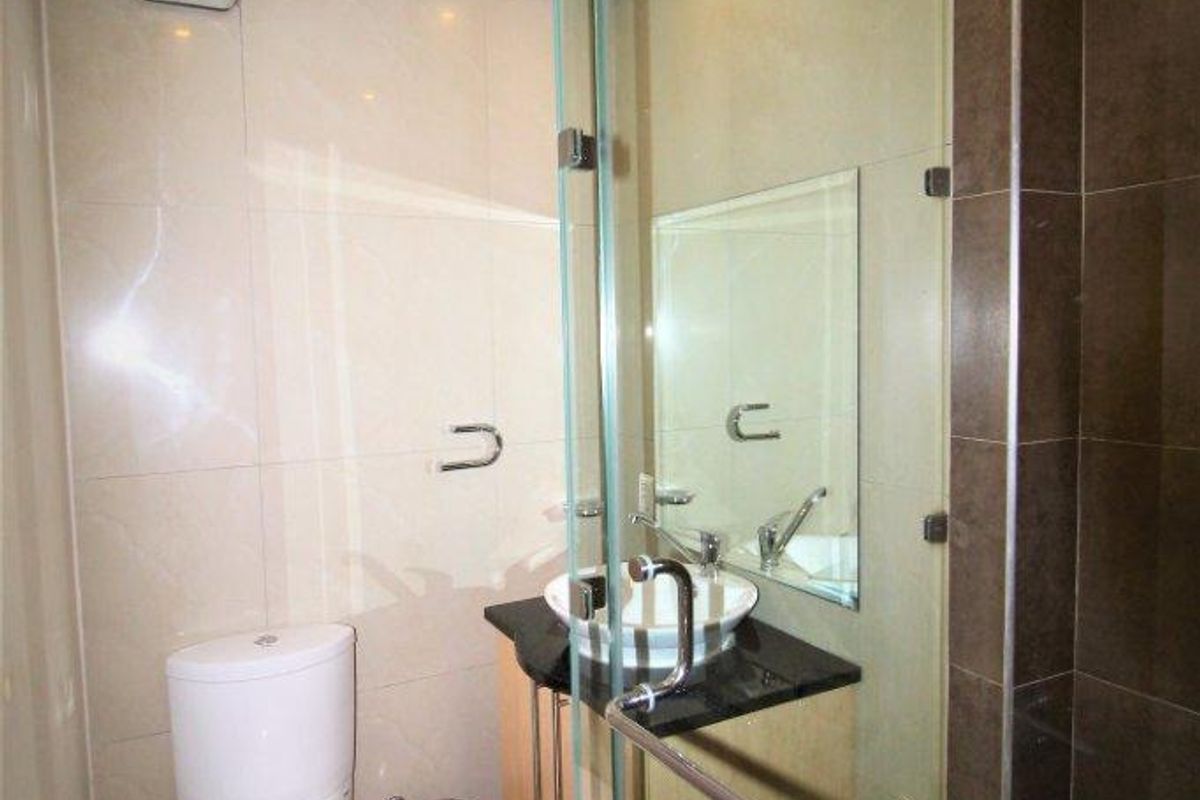 Compact modern bathroom featuring a glass-enclosed shower, vessel sink vanity, and neutral wall and floor tiling.