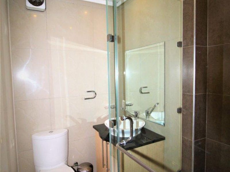 Compact modern bathroom featuring a glass-enclosed shower, vessel sink vanity, and neutral wall and floor tiling.