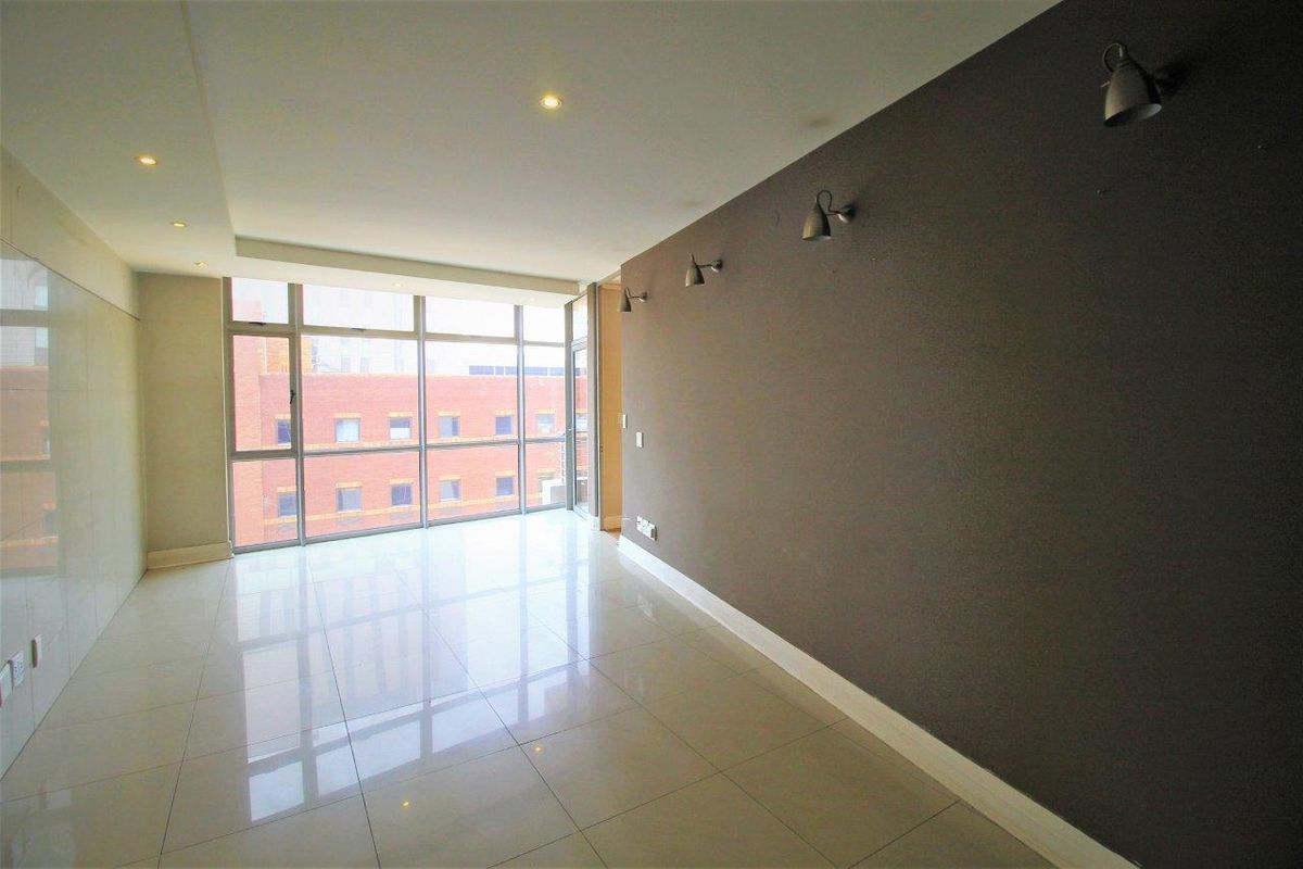 A bright, empty living area featuring polished tiled floors, modern recessed lighting, and large windows providing ample natural light.