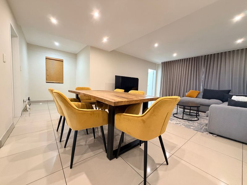 A bright and spacious open-plan living and dining area featuring modern porcelain floor tiles, recessed downlighting, and neutral wall finishes.