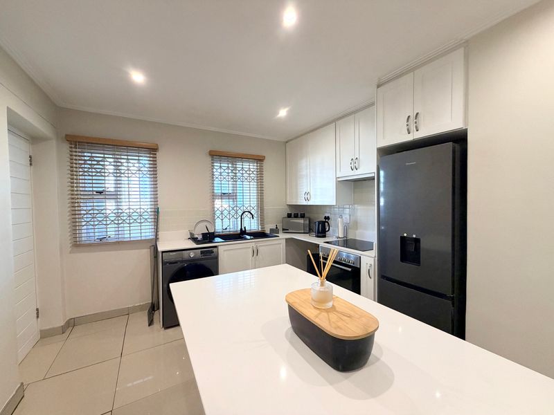 Modern kitchen featuring white cabinetry, quartz countertops, integrated appliances, tiled flooring, and recessed lighting, offering a clean and functional workspace.
