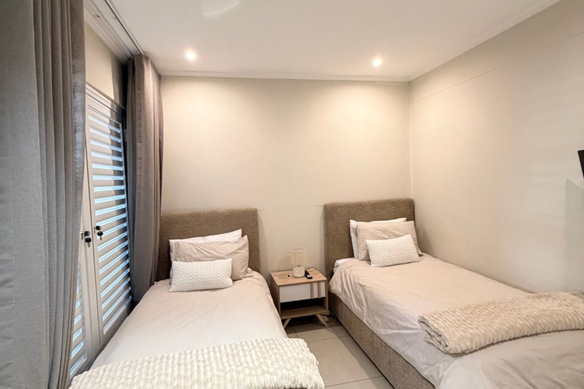 A well-maintained bedroom featuring neutral tiled flooring, recessed downlighting, and a sliding door with integrated shutters for natural light control.