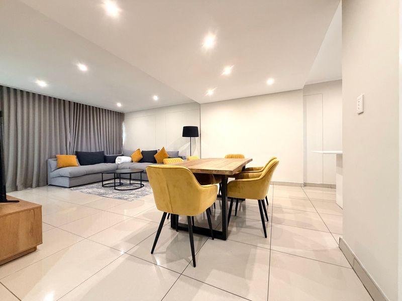 Spacious open-plan living and dining area featuring modern porcelain floor tiles, recessed downlighting, and a large mirrored feature wall.