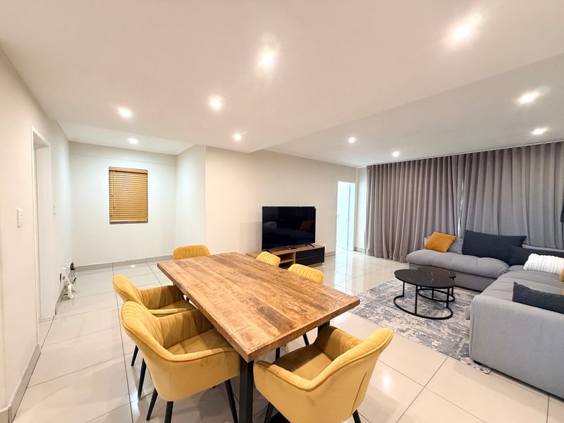 Spacious open-plan living and dining area featuring neutral tiled flooring, recessed downlighting, and large windows dressed with modern curtains and blinds.