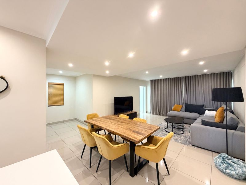 Spacious open-plan living and dining area featuring neutral tiled flooring, recessed downlighting, and large floor-to-ceiling curtains.