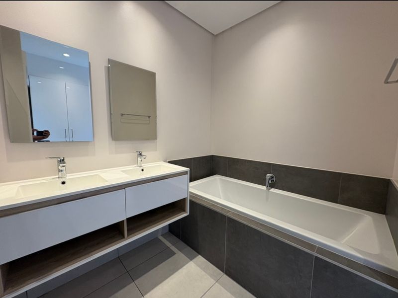 Modern bathroom featuring a sleek double vanity with integrated sinks, wall-mounted mirrors, and a spacious built-in bathtub with contemporary dark tile surround.