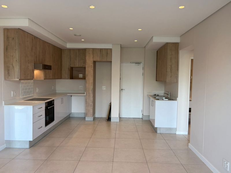 Modern kitchen featuring light wood-tone cabinetry, white countertops, integrated appliances, and tiled flooring in a clean, open-plan layout.