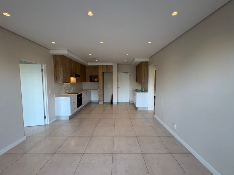 Spacious open-plan kitchen and living area featuring modern cabinetry, integrated appliances, tiled flooring, and recessed lighting in a clean, neutral setting.