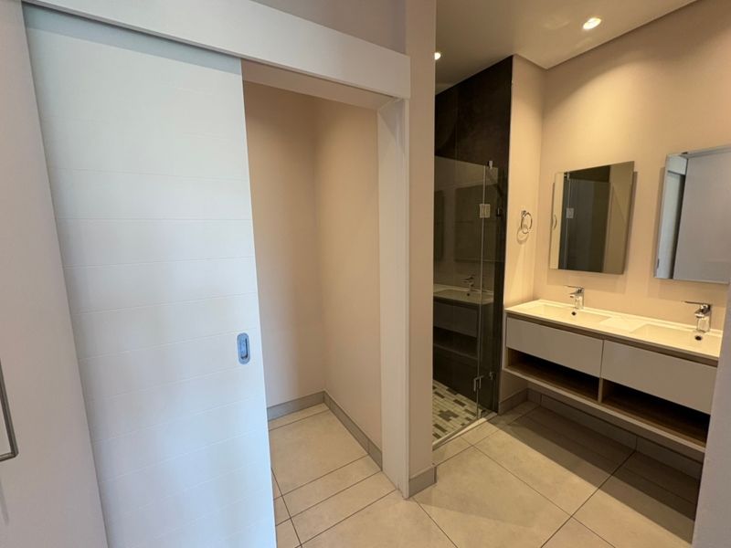 Modern bathroom featuring a double vanity with integrated sinks, a glass-enclosed shower, and a space-saving sliding door.