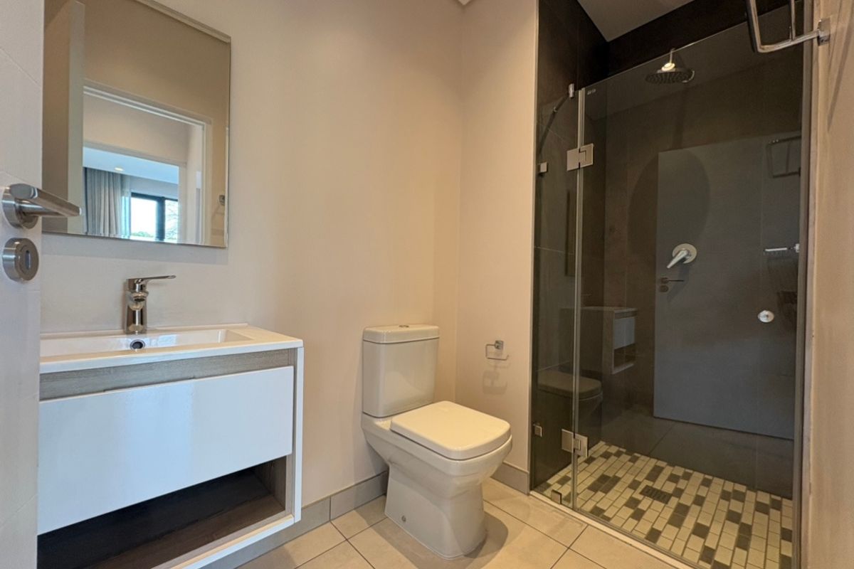 Modern bathroom featuring a sleek vanity with basin, a wall-mounted mirror, a toilet, and a glass-enclosed shower with mosaic floor tiling.