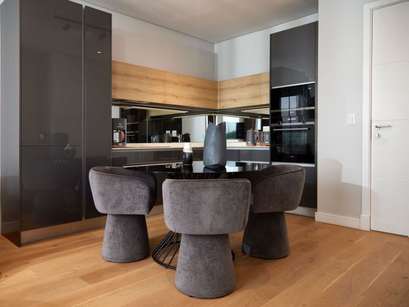Modern kitchen featuring high-gloss cabinetry, integrated oven, mirrored splashback, and warm timber flooring in a sleek, contemporary design.