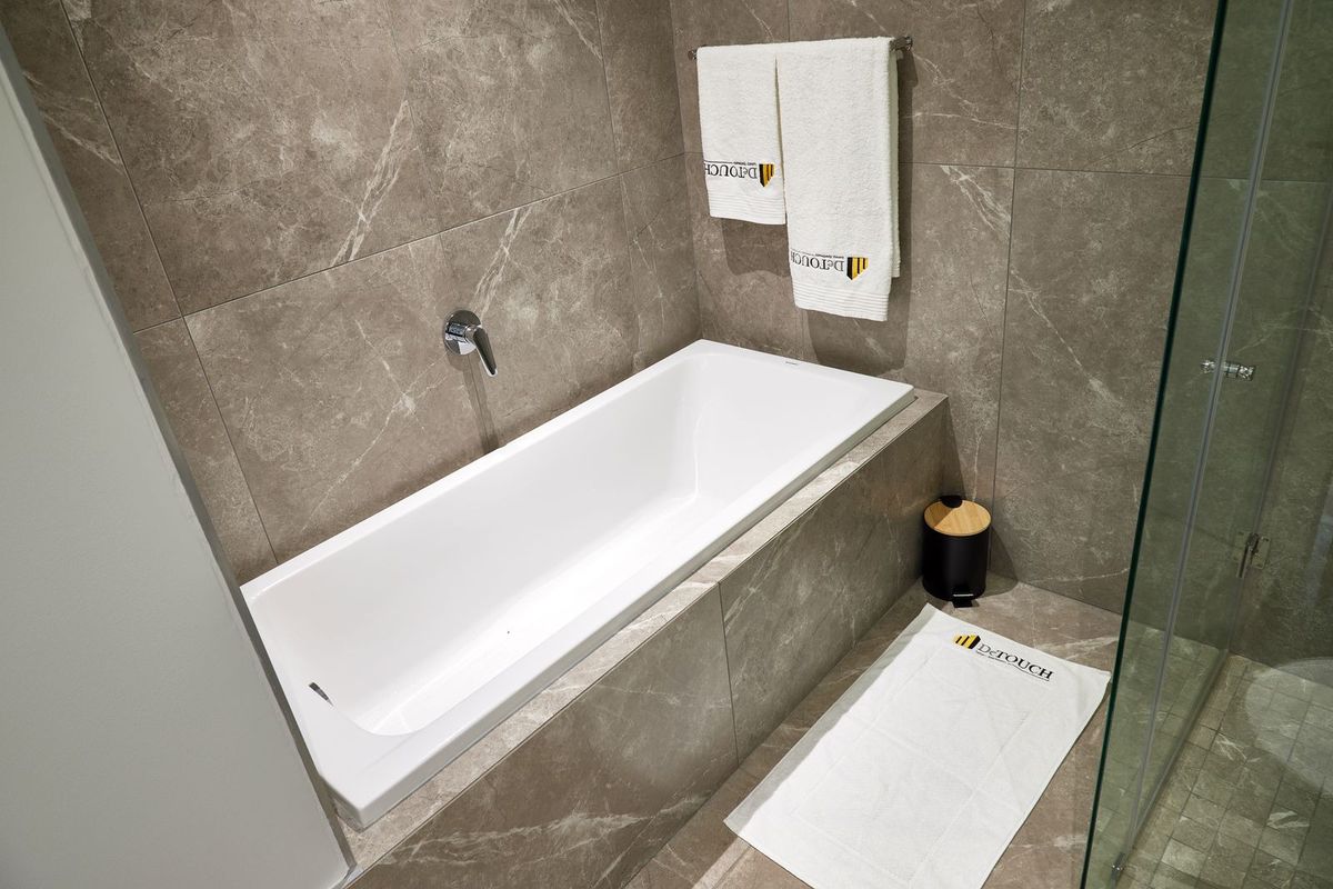 Modern bathroom featuring a sleek built-in bathtub with wall-mounted faucet, complemented by high-quality large format marble-look porcelain wall tiles and a glass shower enclosure.