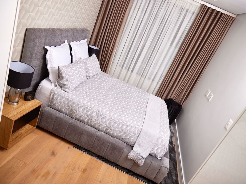 A well-maintained bedroom featuring modern laminate flooring, a textured feature wall, and floor-to-ceiling curtains.