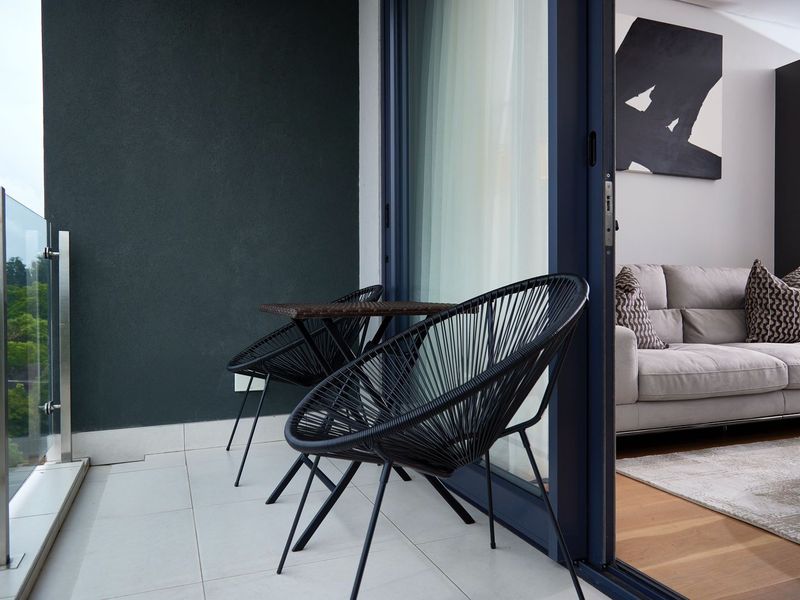 A modern balcony featuring a sleek glass balustrade, tiled flooring, and seamless access to the interior living area through a large sliding glass door.