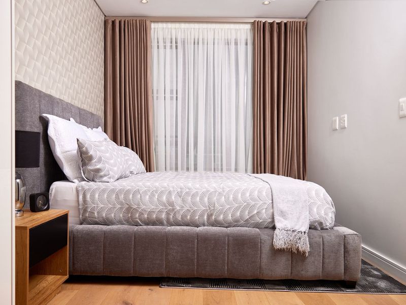 A well-appointed bedroom featuring timber flooring, a textured feature wall, and recessed downlighting, creating a modern and comfortable living space.