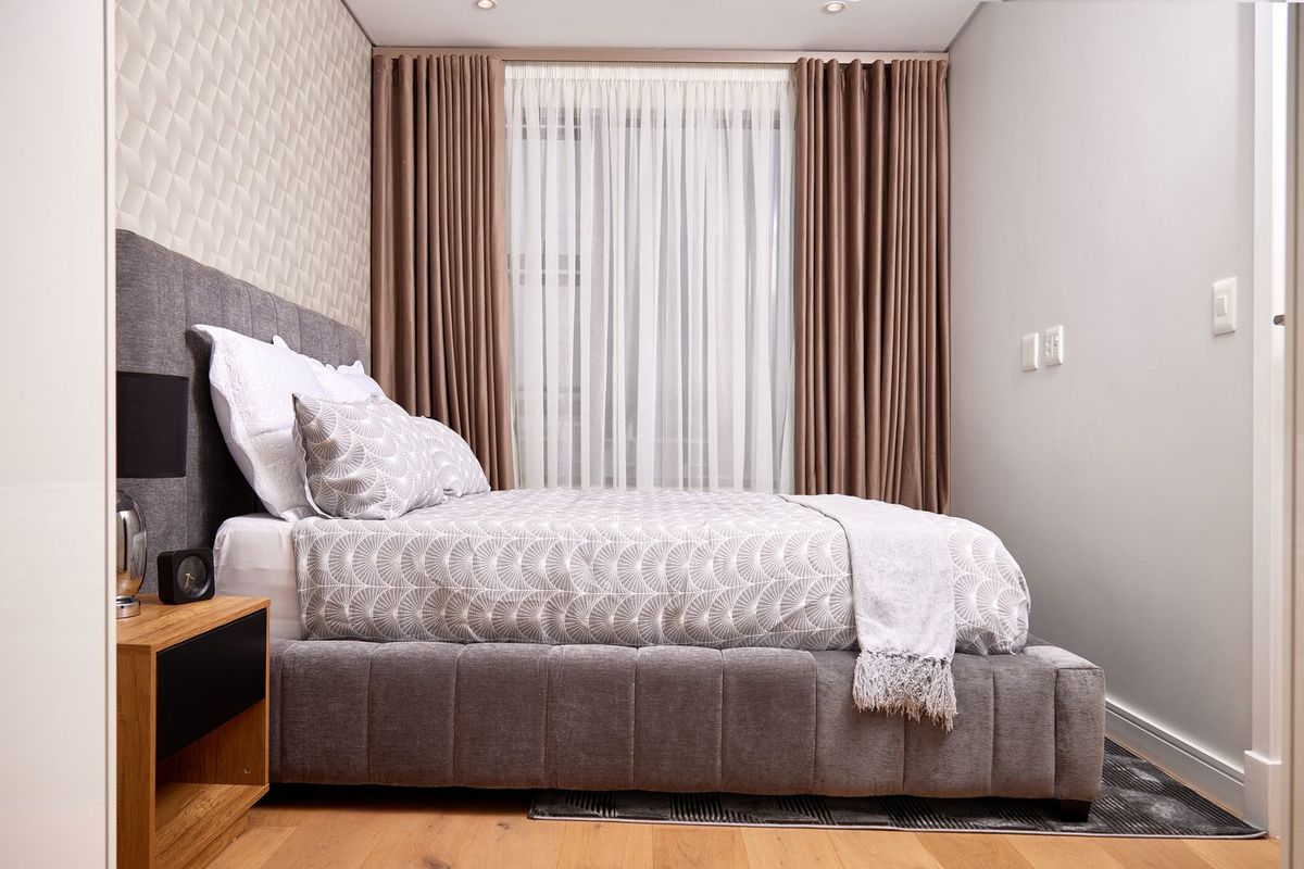 A well-appointed bedroom featuring timber flooring, a textured feature wall, and recessed downlighting, creating a modern and comfortable living space.