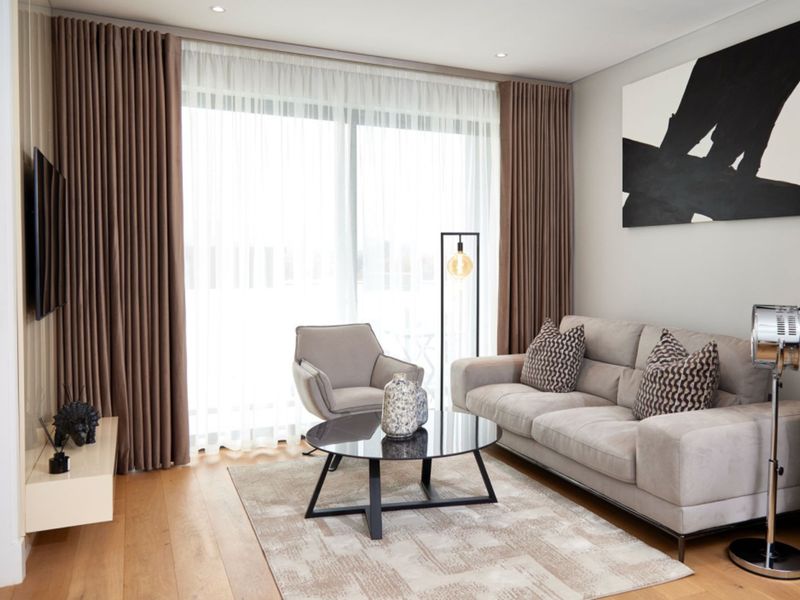 A modern, well-maintained living room featuring hardwood flooring, recessed lighting, and a large sliding glass door with floor-to-ceiling curtains.