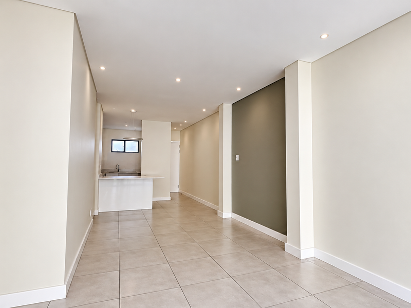 A bright, modern open-plan living and kitchen area featuring neutral tones, tiled flooring, and recessed lighting, offering a clean and versatile space.