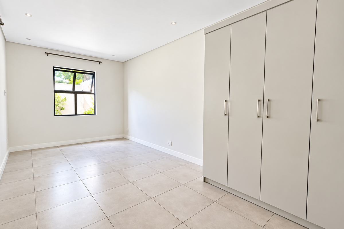 A bright and spacious bedroom featuring neutral tiled flooring, recessed downlights, and ample built-in cupboard storage.