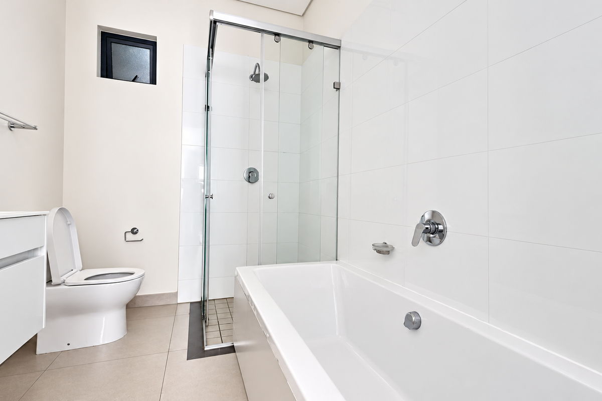 A modern, clean bathroom featuring a glass-enclosed shower, a white bathtub, a wall-mounted vanity, and a toilet with neutral floor and wall tiling.