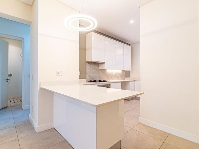 Modern kitchen featuring sleek white cabinetry, stone countertops, a breakfast bar, and integrated gas hob, finished with neutral floor tiles.