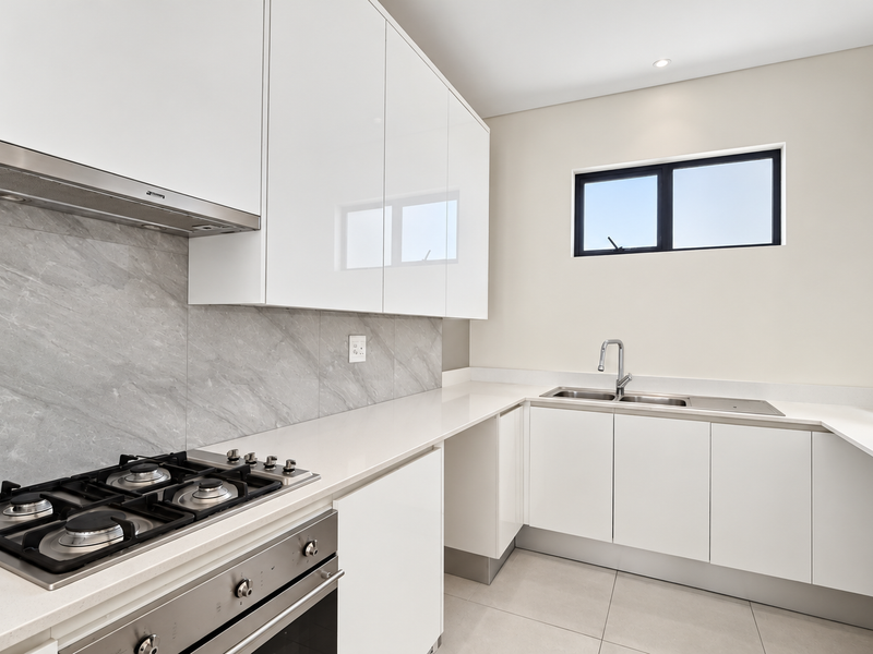 Modern kitchen featuring high-gloss white cabinetry, stone countertops, a gas cooktop with extractor, and a double bowl sink with a sleek mixer tap.