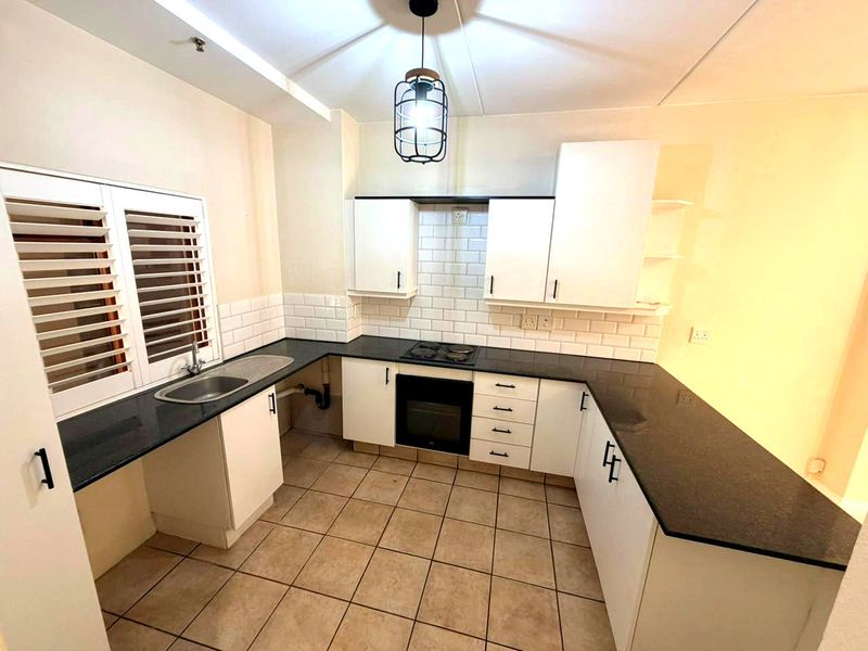 A functional kitchen featuring white cabinetry, dark granite countertops, subway tile backsplash, built-in oven, and hob, complemented by tiled flooring and shutter blinds.