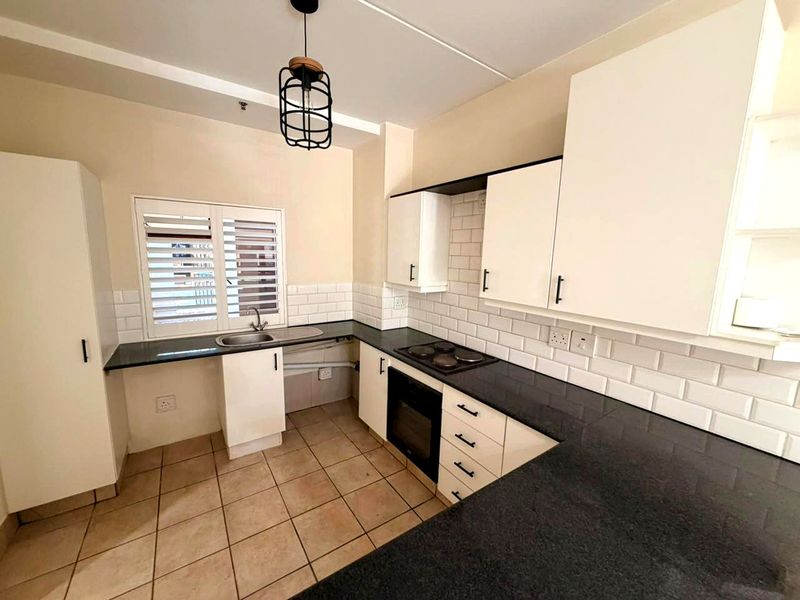 A clean, functional kitchen featuring white cabinetry, dark granite countertops, subway tile backsplash, and built-in oven with electric hob.