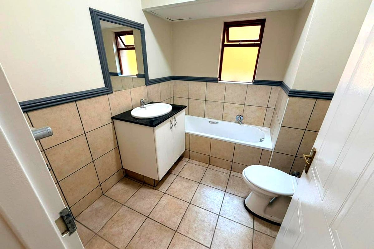 A functional bathroom featuring a vanity with basin, bathtub, toilet, and neutral wall and floor tiling.