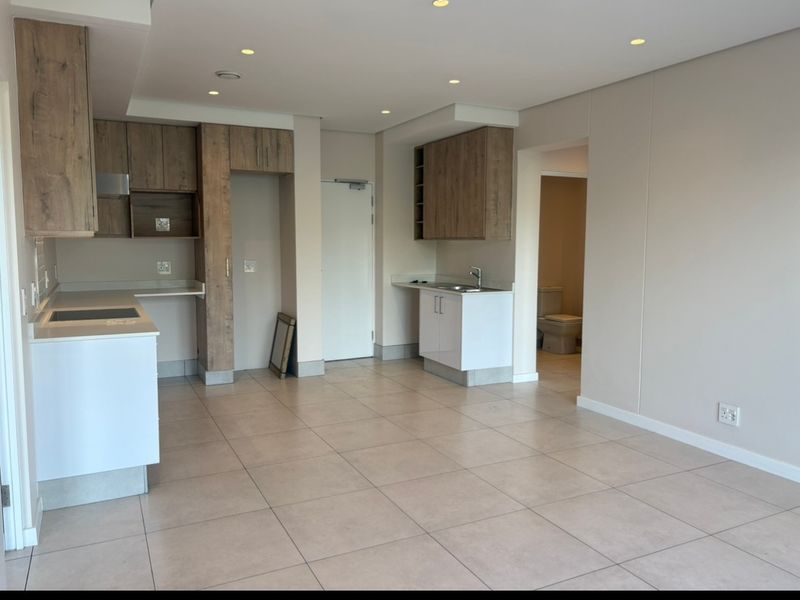 An open-plan kitchen and living area featuring modern wood-look cabinetry, stone countertops, tiled flooring, and recessed lighting, with an adjacent bathroom visible.
