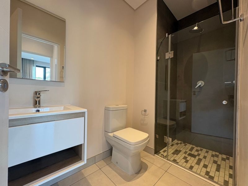 Modern bathroom featuring a sleek vanity with basin, a wall-mounted mirror, a toilet, and a glass-enclosed shower with mosaic floor tiling.