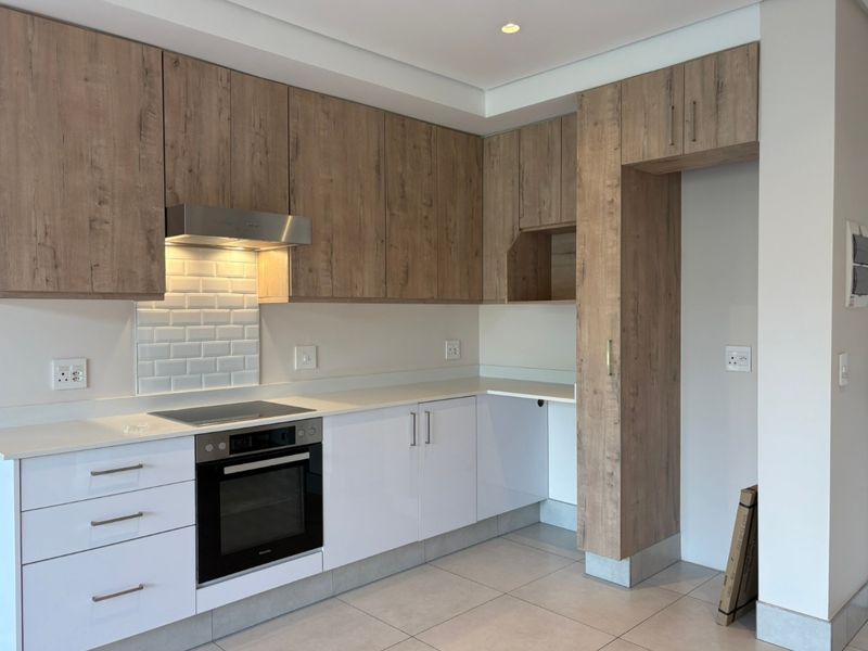 Modern kitchen featuring wood-grain and white cabinetry, stone countertops, subway tile backsplash, and integrated appliances including an oven and electric hob.