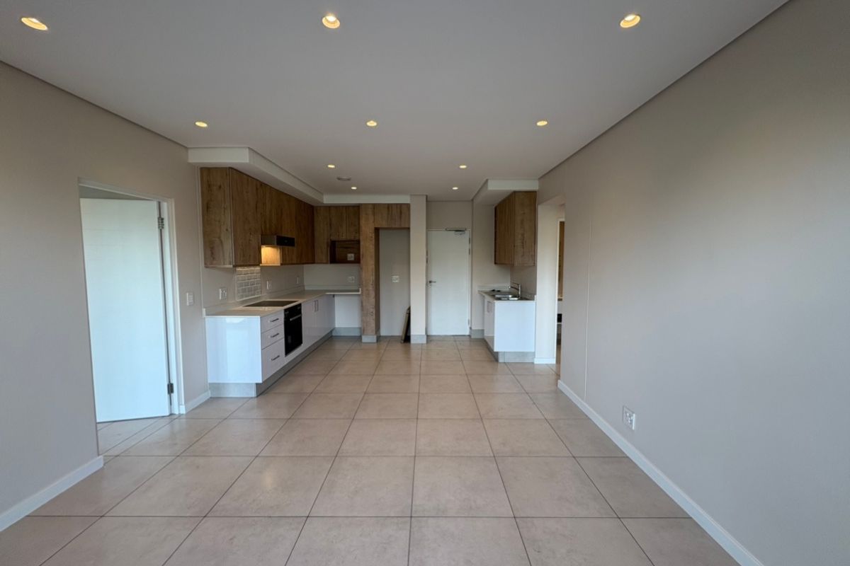 Spacious open-plan kitchen and living area featuring modern cabinetry, integrated appliances, tiled flooring, and recessed lighting in a clean, neutral setting.