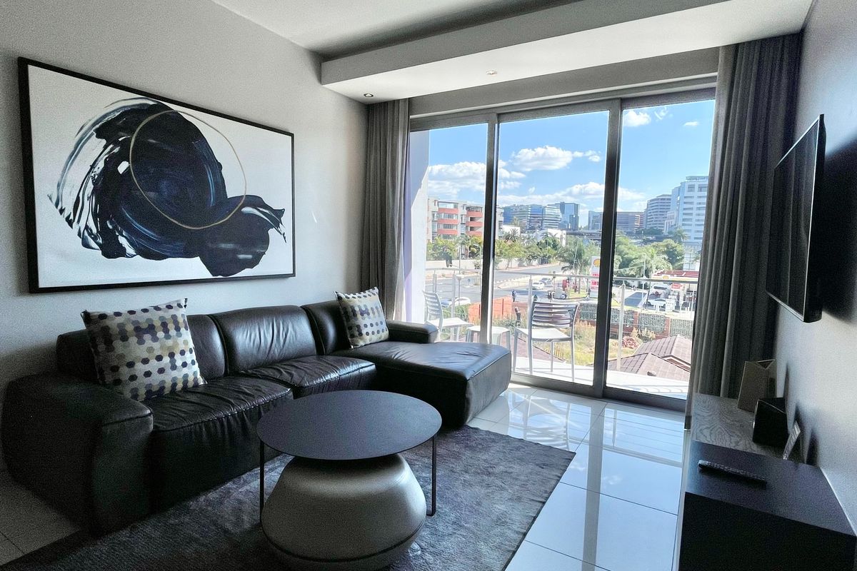 Modern living room featuring large sliding glass doors that open to a balcony with urban views, complemented by polished floor tiles and recessed lighting.