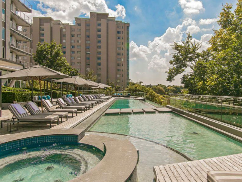 A well-maintained outdoor pool area featuring a swimming pool, integrated jacuzzi, timber decking, and modern glass balustrades overlooking the surrounding landscape.