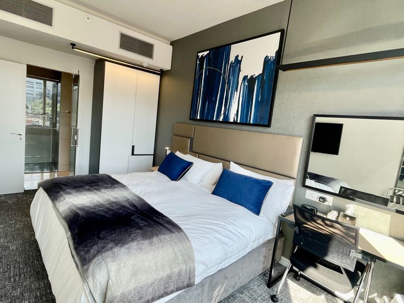 Modern bedroom featuring a built-in wardrobe, integrated desk, upholstered headboard, and ducted air conditioning in a well-maintained contemporary apartment.