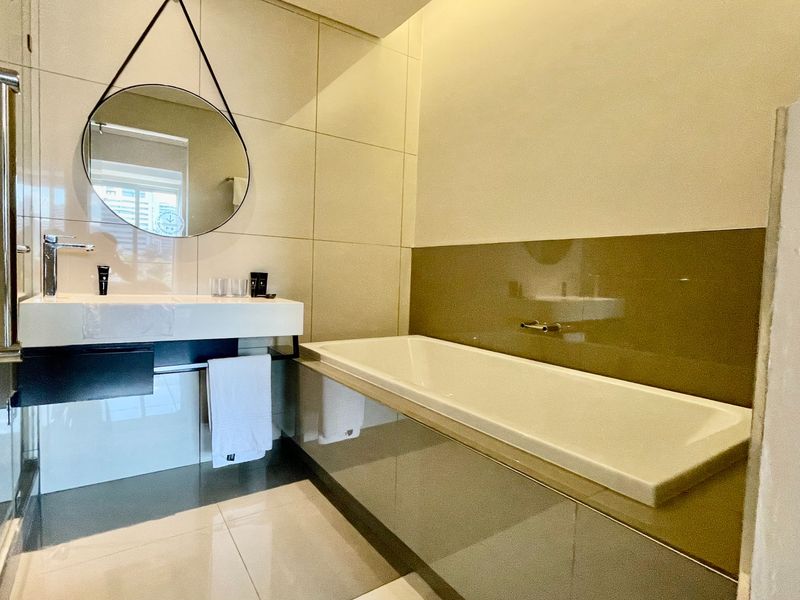 Modern bathroom featuring a sleek wall-mounted vanity, built-in bathtub with tiled surround, and contemporary large-format wall tiles.