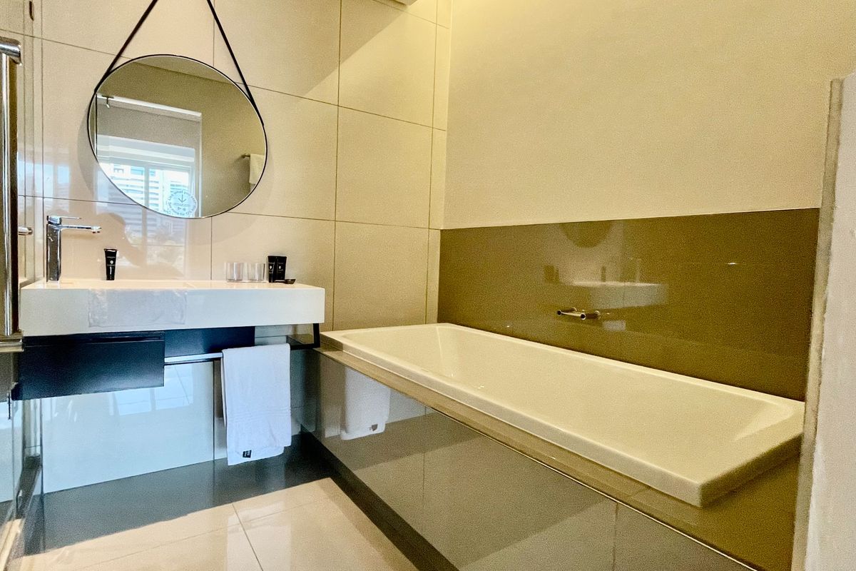 Modern bathroom featuring a sleek wall-mounted vanity, built-in bathtub with tiled surround, and contemporary large-format wall tiles.